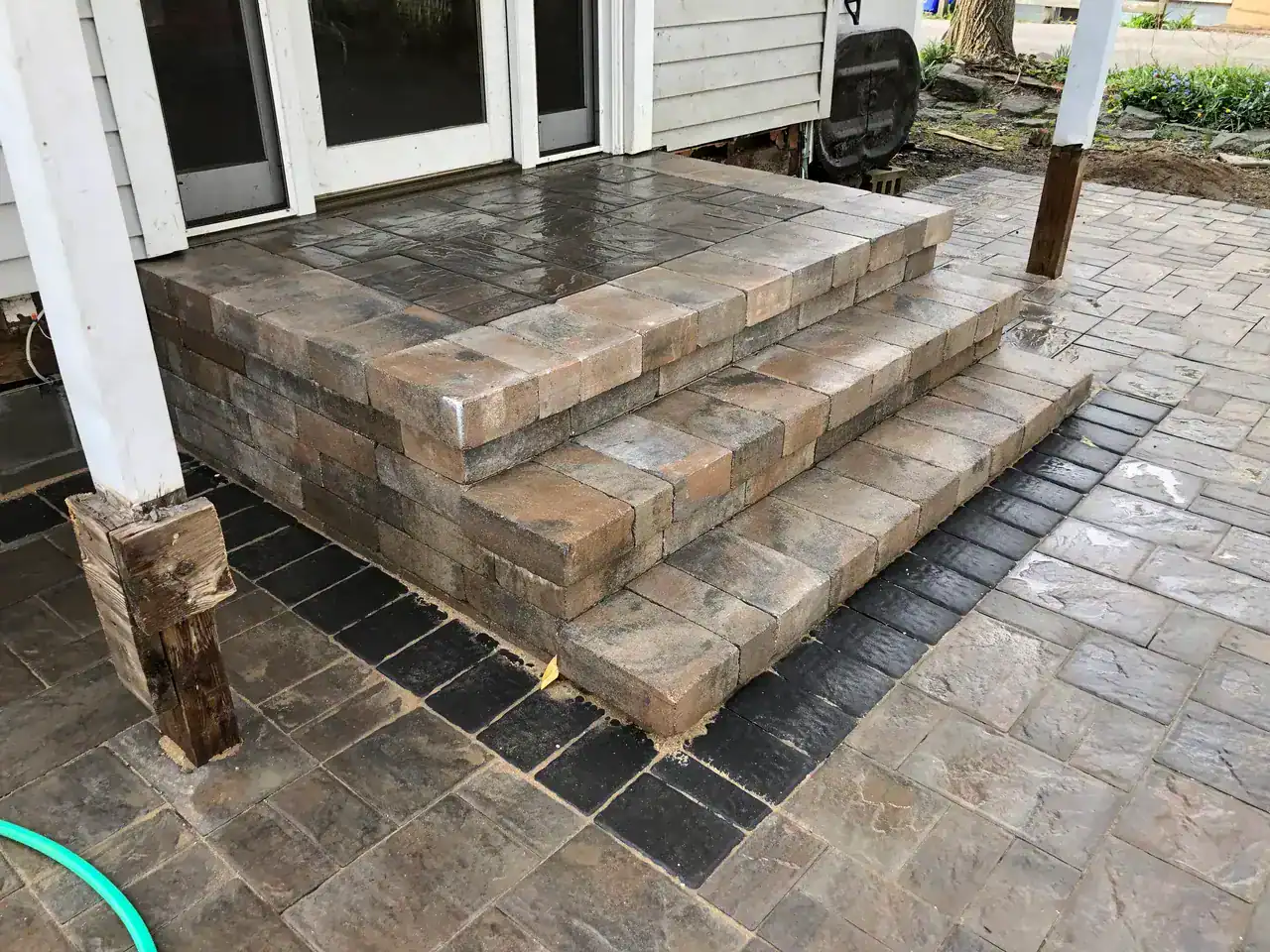 Wet stone steps, crafted by expert Masonry Contractors Suffolk & Nassau County, lead to a patio door.